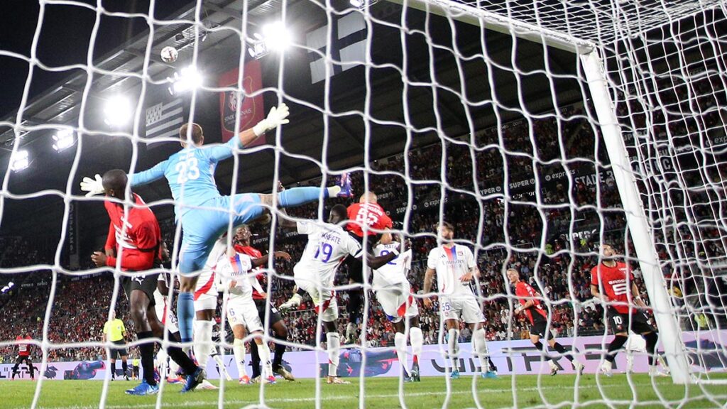 Action entre Rennes et Lyon vue depuis l'arrière du but lyonnais avec le gardien de l'OL effectuant un saut et grand écart