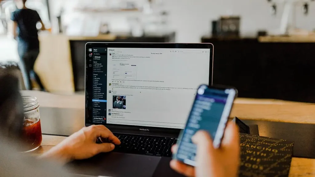 Photo montrant un ordinateur portable allumé et une main tenant un smartphone, illustration sur le thème de la communication digitale